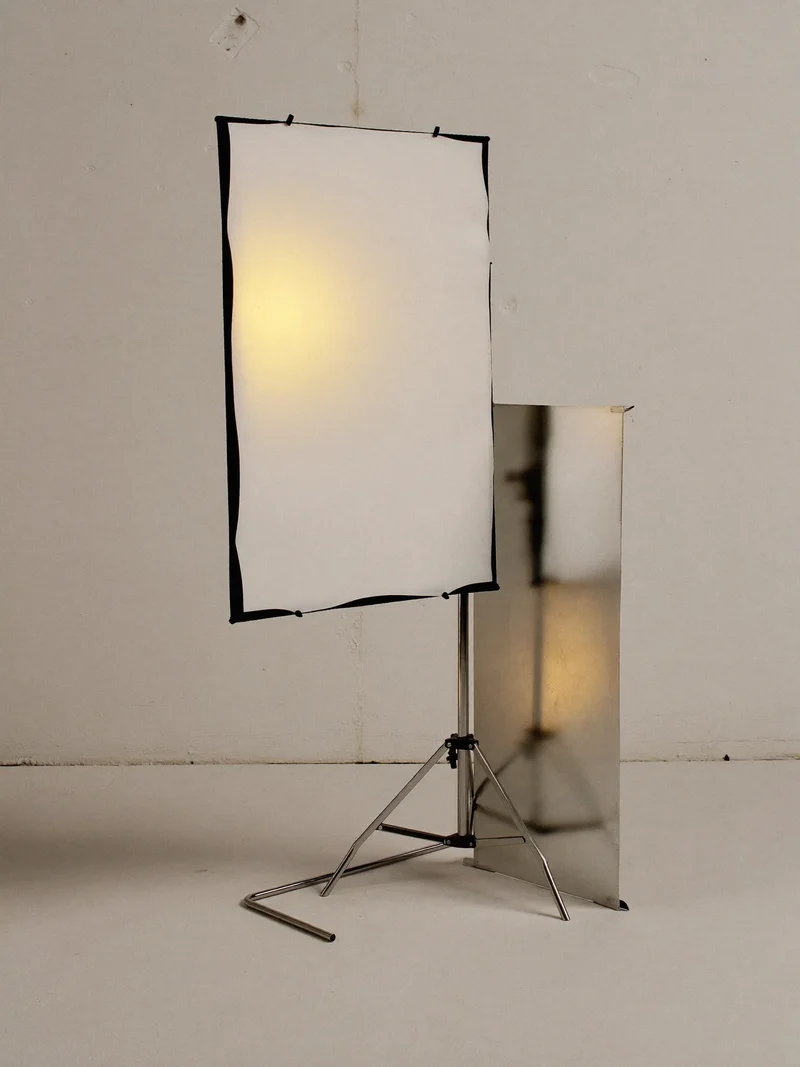LED-Panel mit Diffusor auf Lampenstativ, daneben ein gefalteter Reflektor